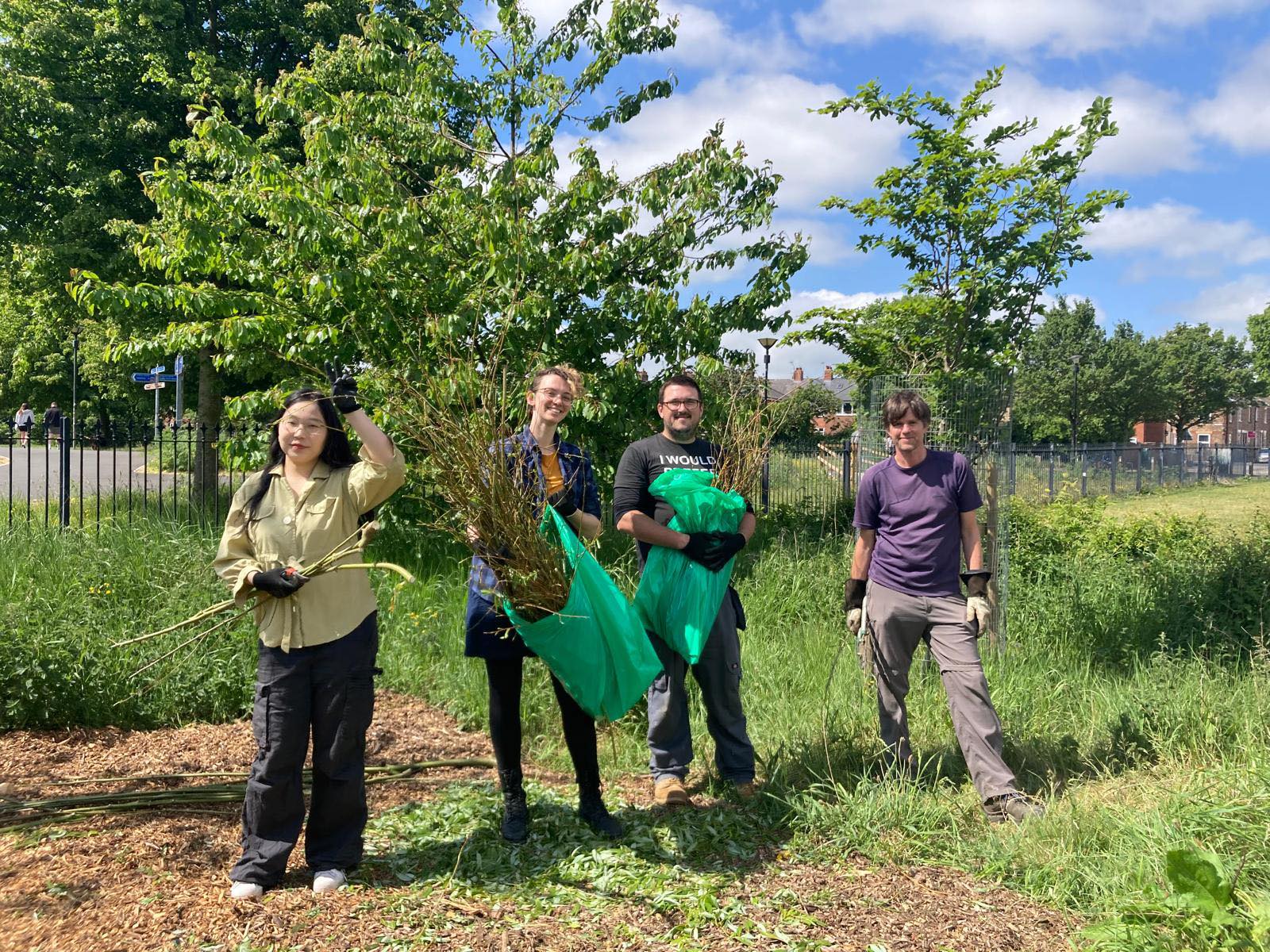 Four people stand in front of a tree at Rowntree Park, carrying garden shears and garden waste