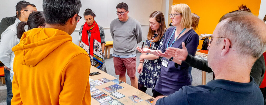 A group of people are gathered around a table with picture cards on - they are taking part in a climate freak workshop