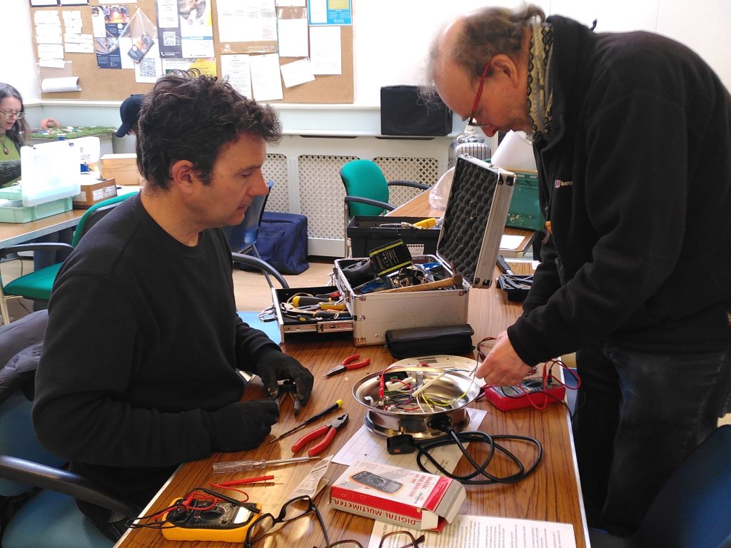 Two men are leaning over a desk covered in various equipment. They are learning how to repair them.