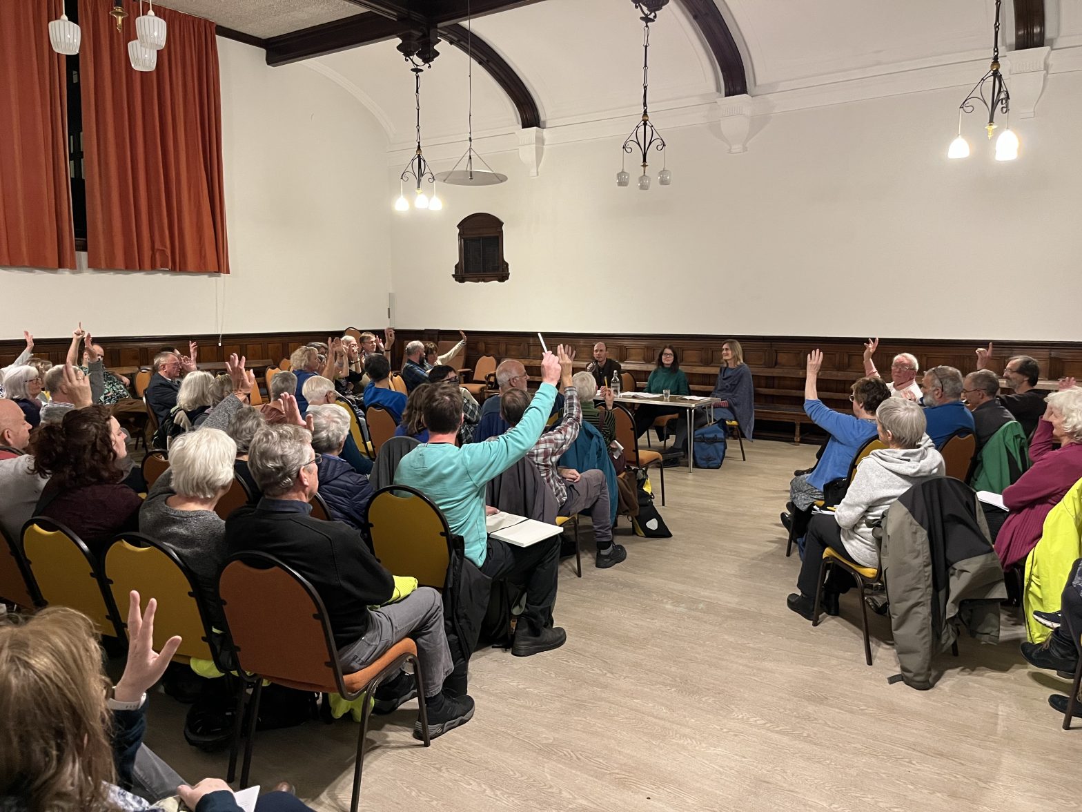 A hall filled with people, some have their hands raised.